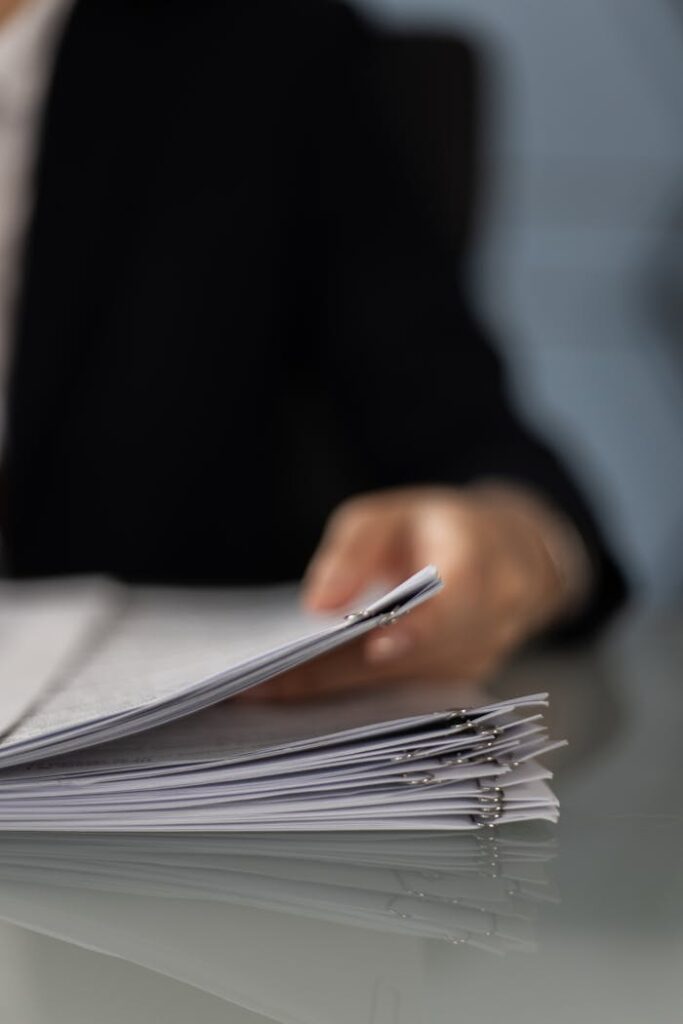 close-up-shot-of-a-person-holding-paperwork-6077587 Blurred hand holding a stack of documents on a glass desk with focus on papers.