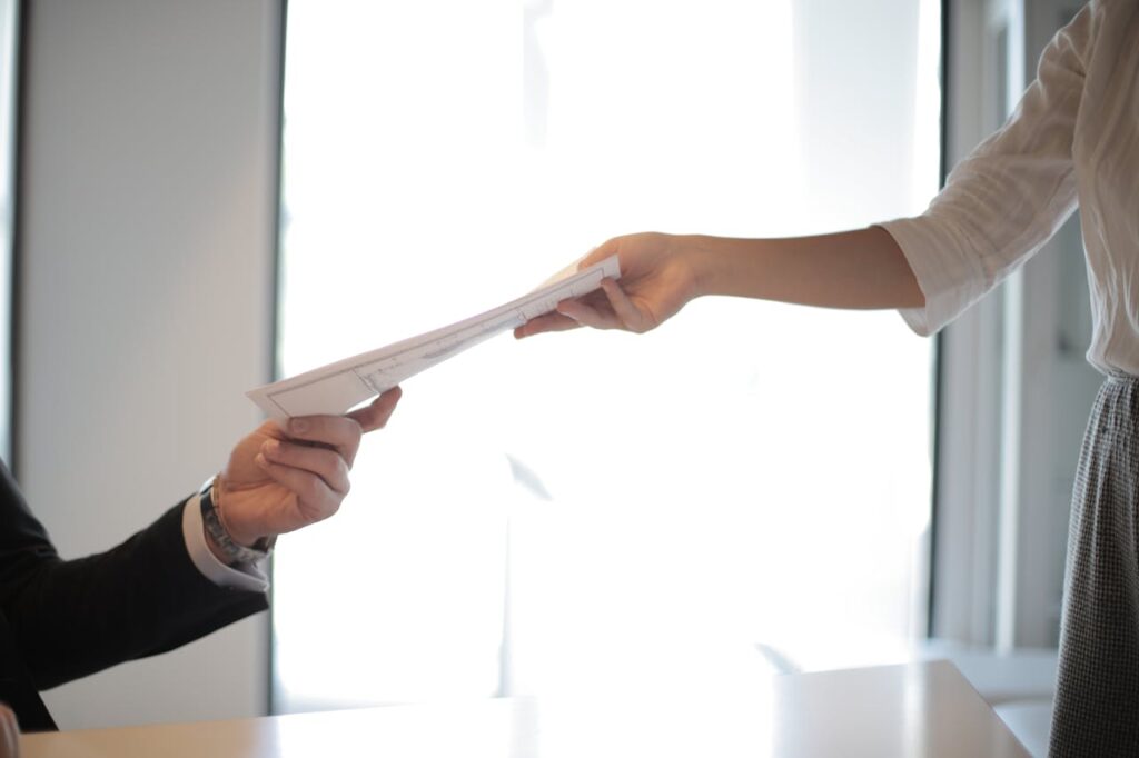 job-applicant-passing-her-documents-3760072 Close-up of hands exchanging documents in a business setting indoors.